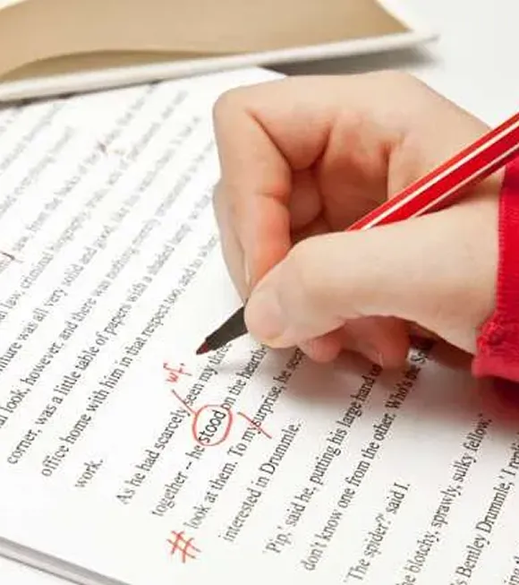 A person writes on paper with a red pen, focusing intently on their task.